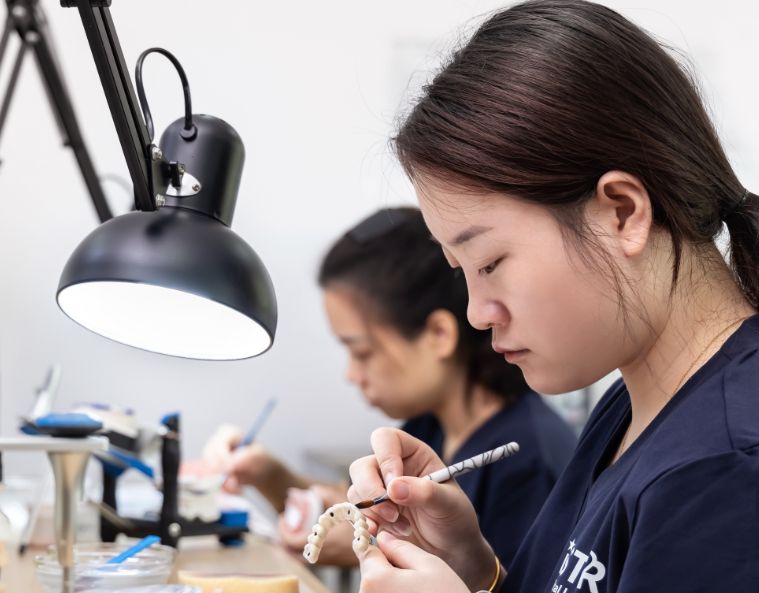 Técnico dental realizando el acabado manual de una corona dental en un área de producción de un laboratorio dental
